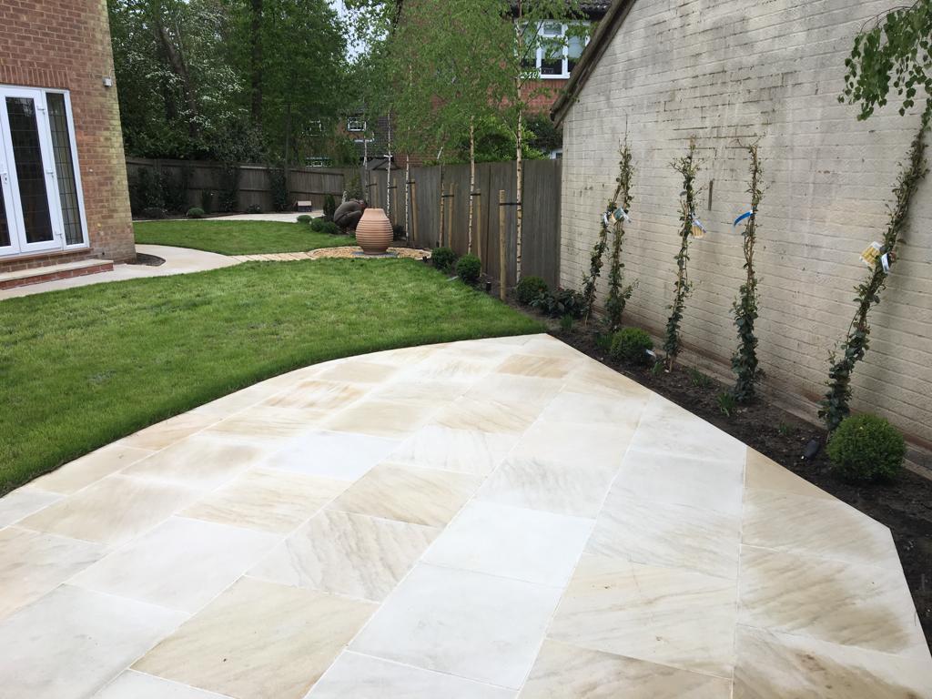 Buff sandstone patio with planted wall border and curved lawn, Surrey