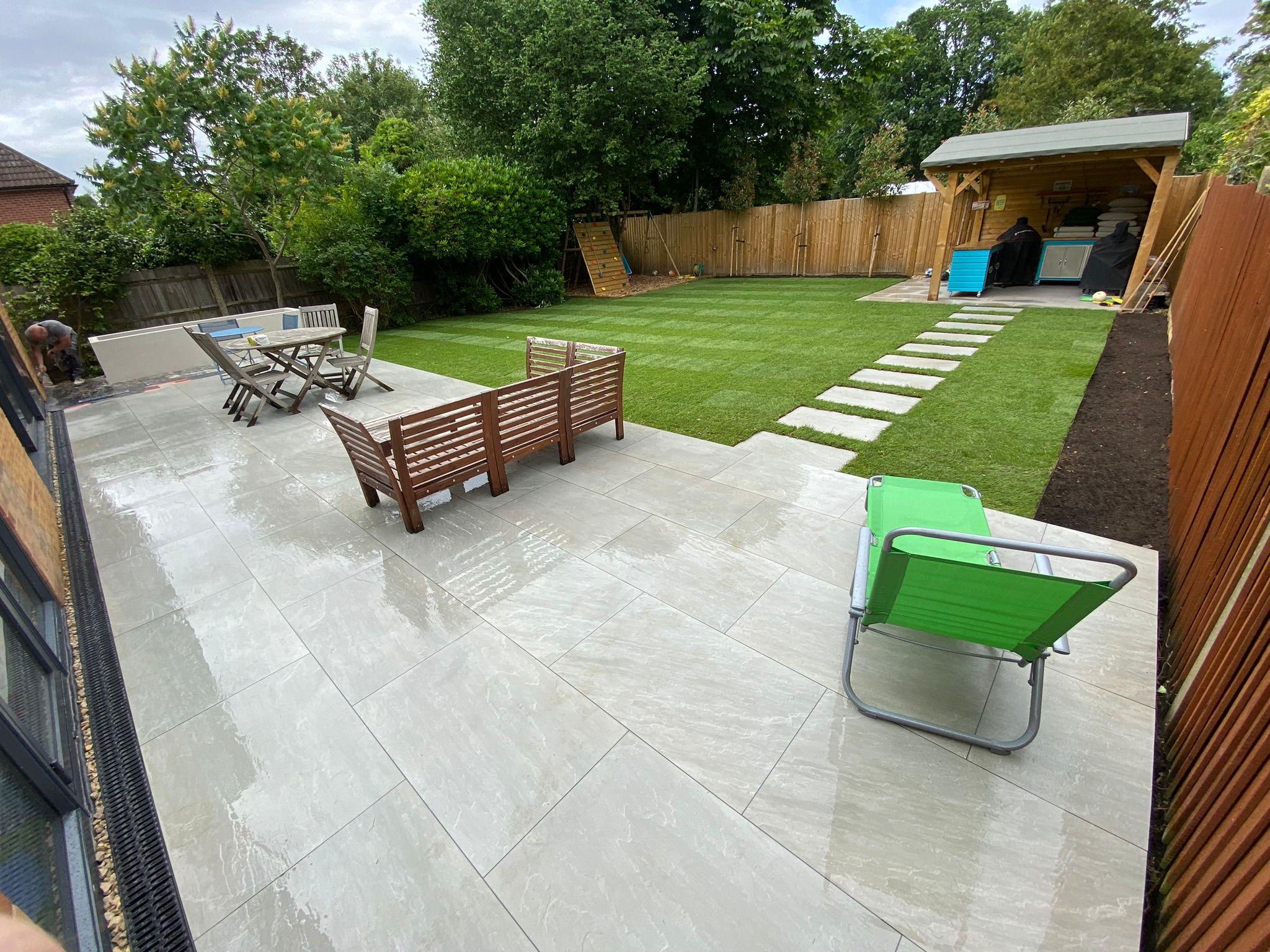 Large grey porcelain patio with outdoor furniture and new turf, Surrey